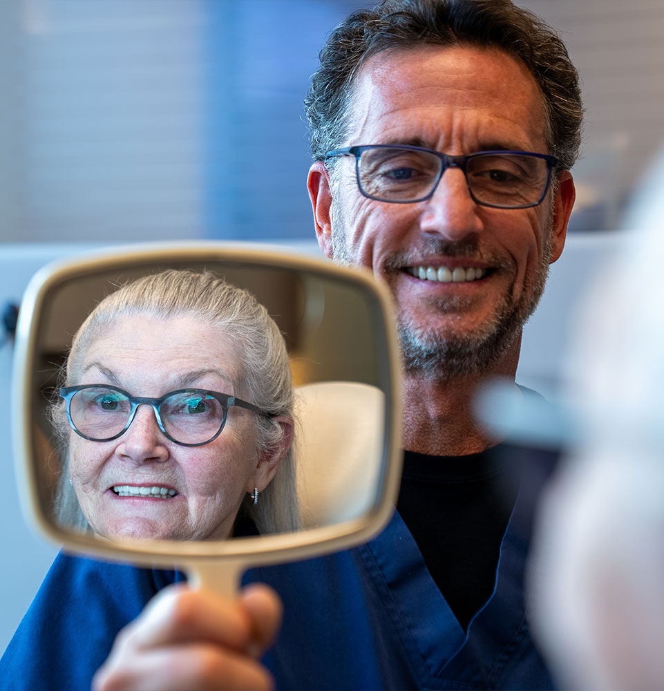 patient smiling brightly while looking in the mirror with doctor
