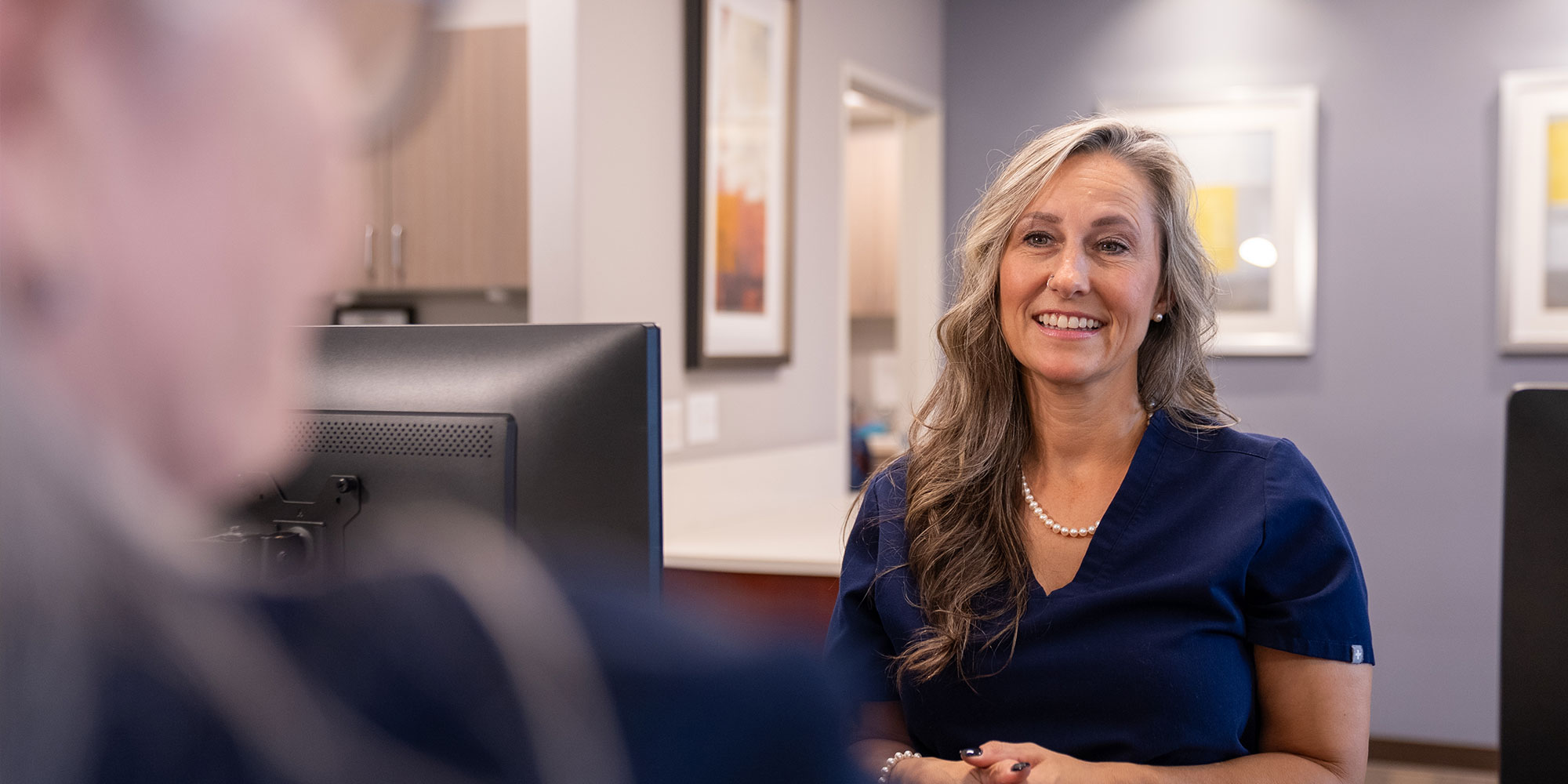 staff member smiling brightly while helping dental implant patient at the front desk of the dental center